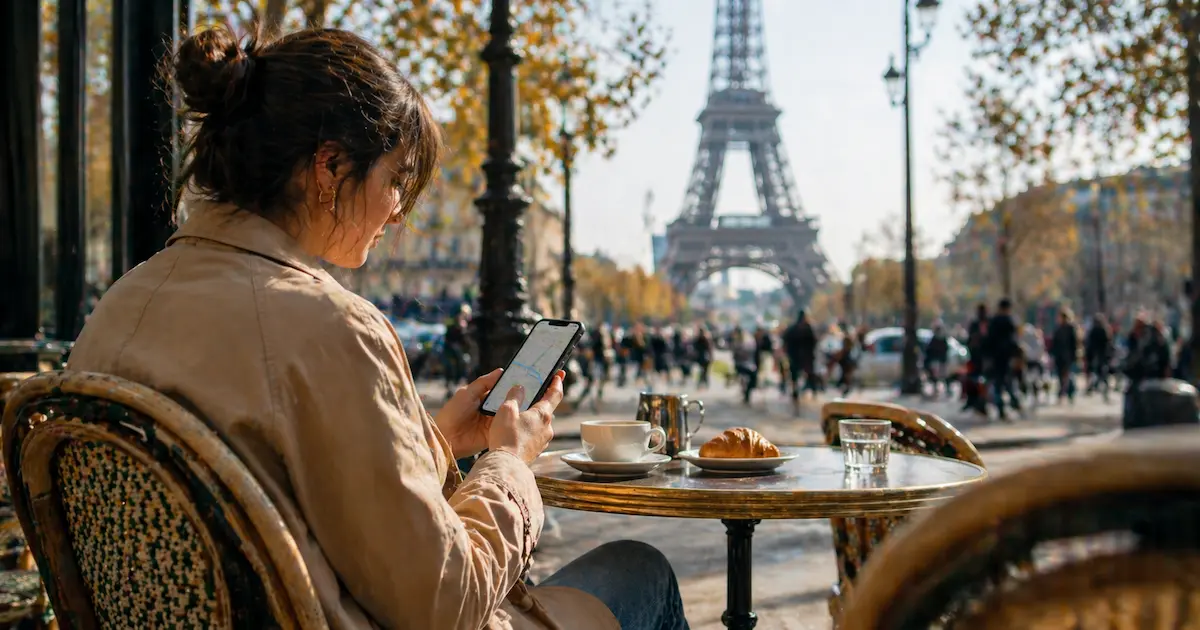 traveler using smartphone at Paris cafe near Eiffel Tower checking maps and apps during the day